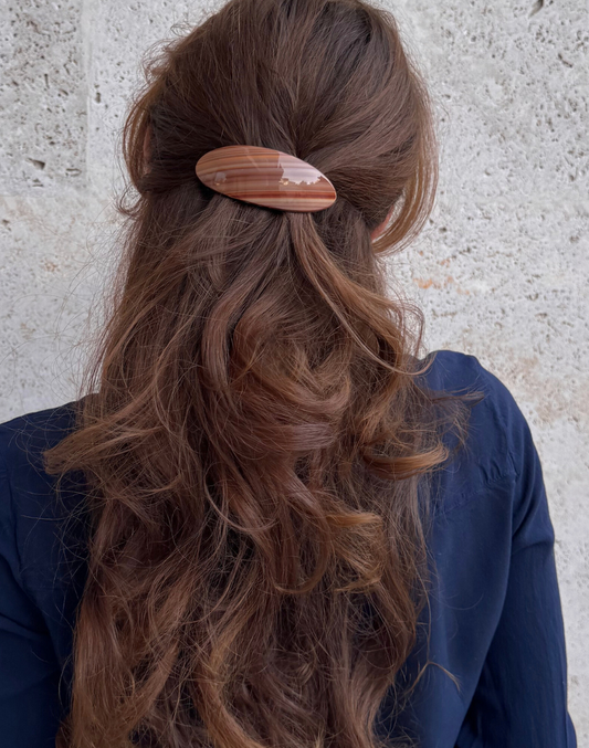 Person with long wavy hair wearing a wooden hair clip against a neutral background