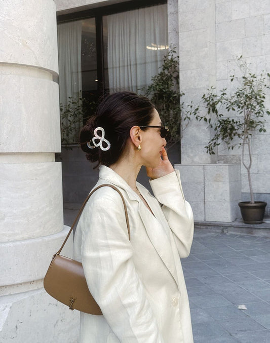 Woman in a white coat with a brown handbag standing against a building exterior