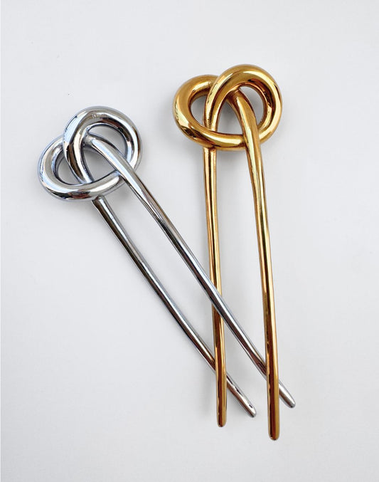 Two metal hair pins with interlocking circular knot tops, one in polished silver and one in polished gold