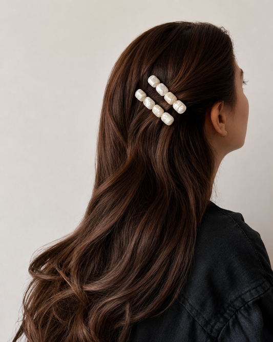 Person with long, wavy hair wearing a hair clip with pearls on a neutral background