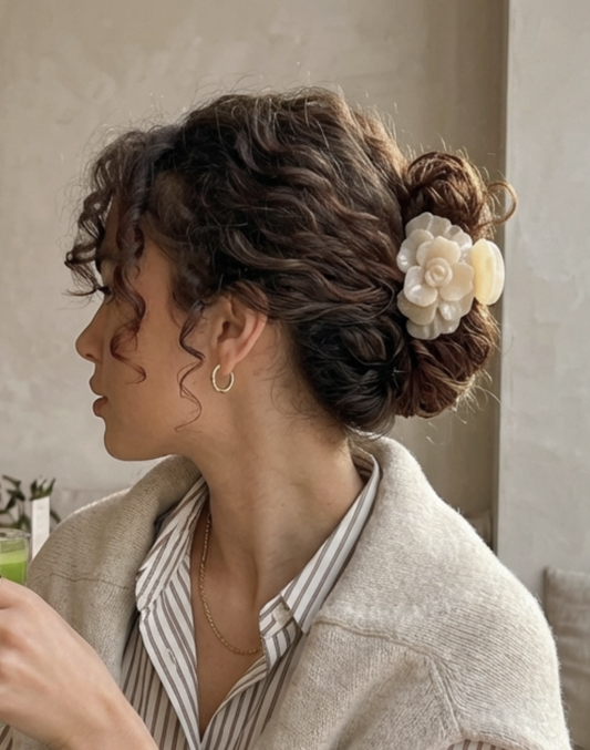 Woman with styled hair featuring a decorative flower, wearing a beige cardigan and striped shirt.