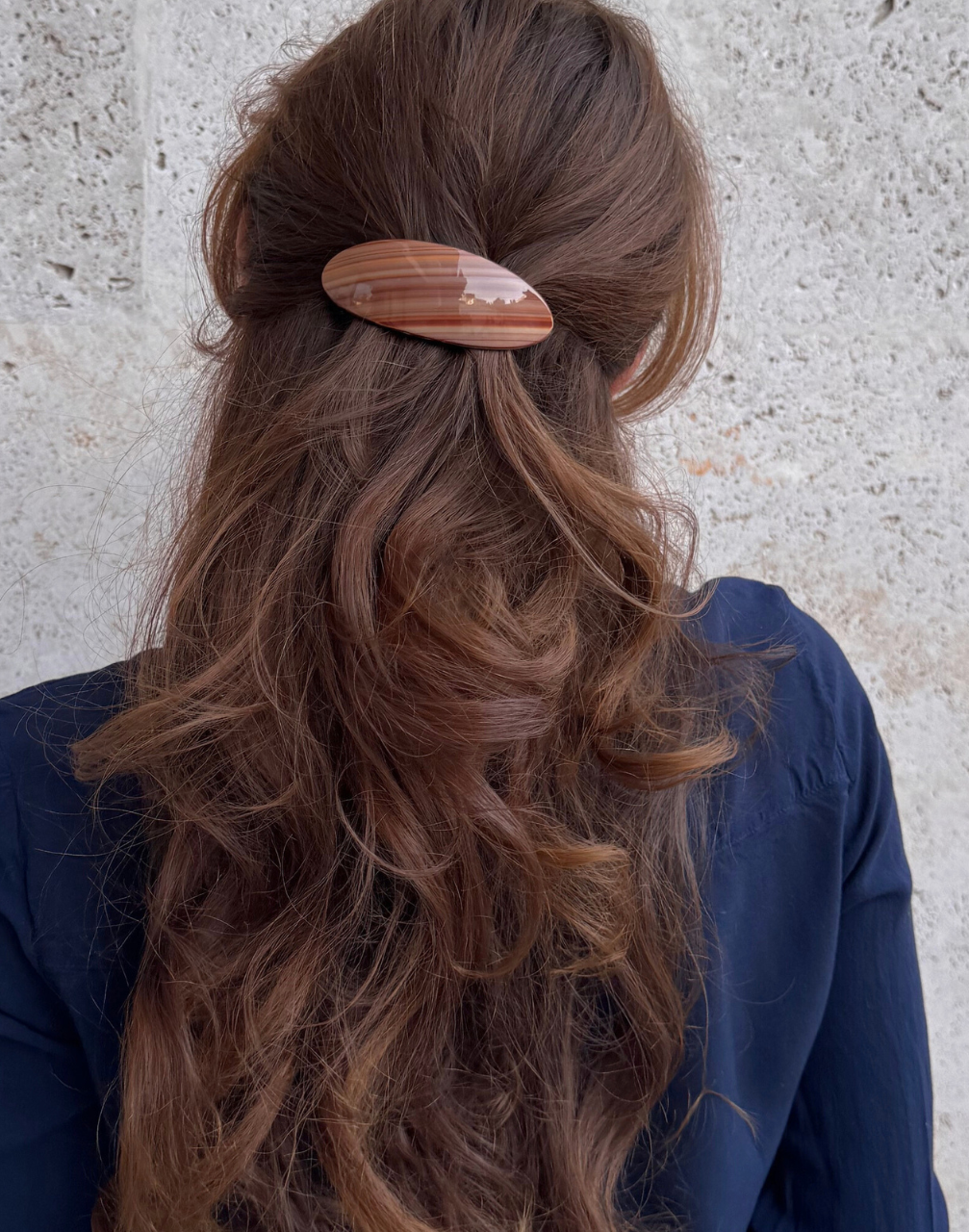 Person with long wavy hair wearing a wooden hair clip against a neutral background