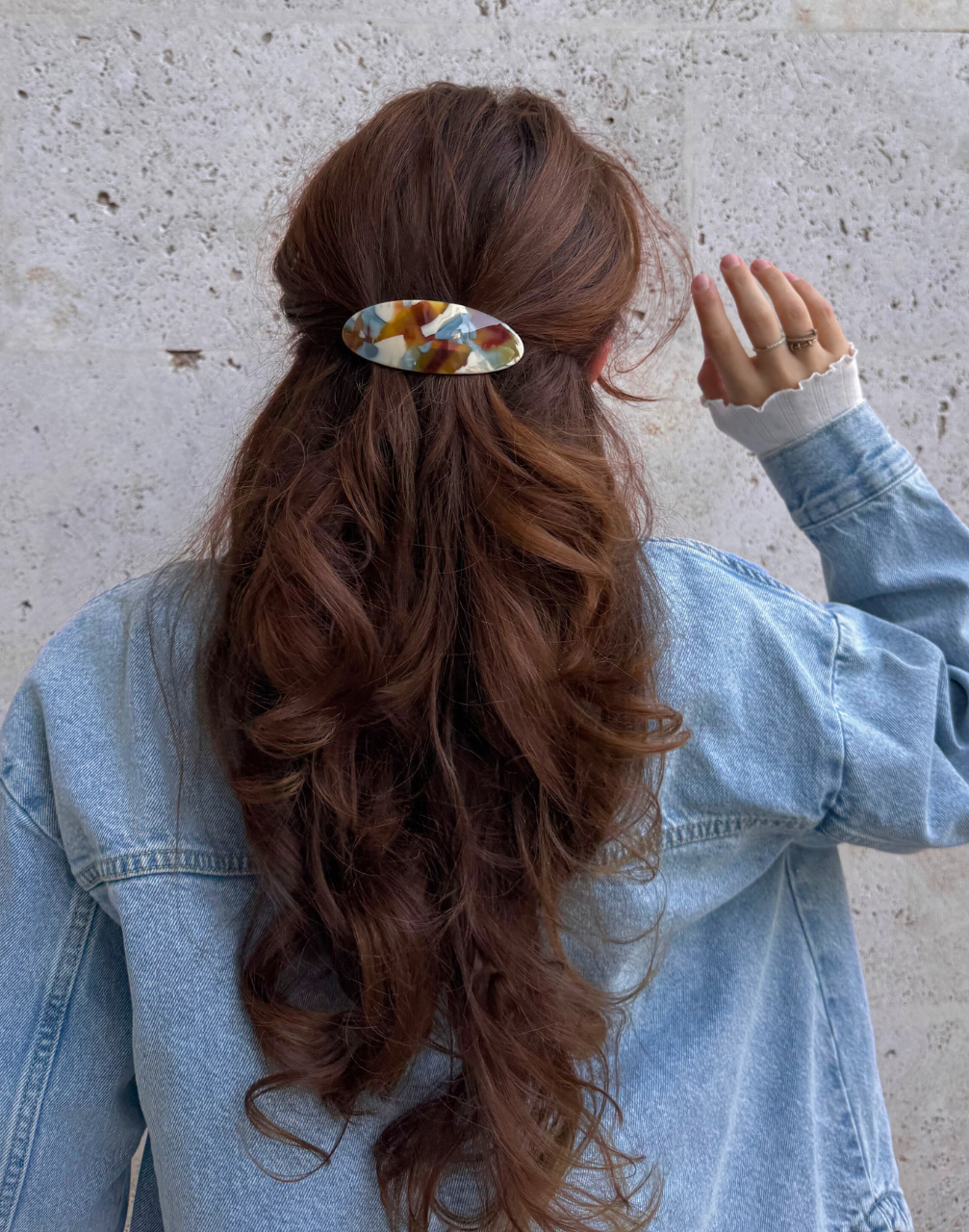 Person with long, wavy hair wearing a colorful hair clip against a neutral background
