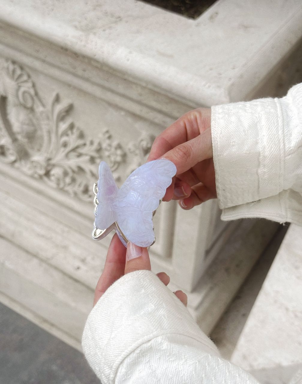 Person holding a butterfly-shaped object in front of a decorative stone wall.