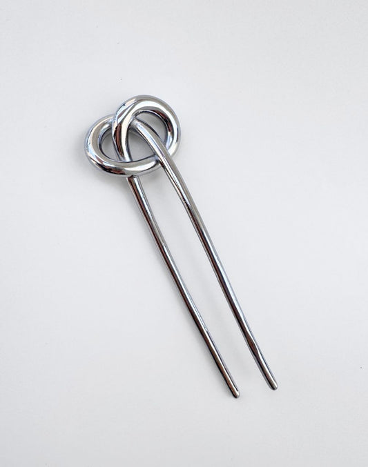 A polished silver metal hair pin with a double-loop knot design at the top and two long straight prongs,